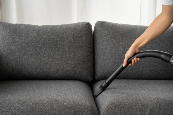 Unrecognizable Asian man housekeeper using a vacuum machine vacuuming a dust on a sofa in living room close up. A man cleaning and sanitizing his house for hygiene living. Vacuum machine and housework - Фото, изображение