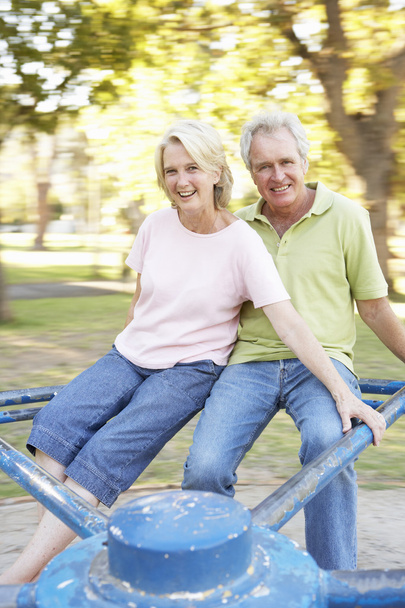 Senior Couple Riding On Roundabout In Park - Foto, afbeelding
