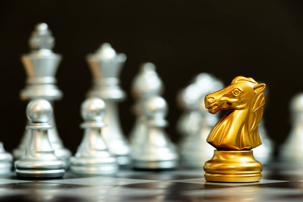 Gouden ridder in schaakspel geconfronteerd met het andere zilveren team op zwarte achtergrond (Concept voor bedrijfsstrategie, zakelijke overwinning of beslissing) - Foto, afbeelding
