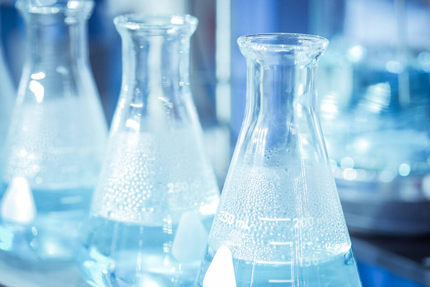 Chemikalien-Reagenzglas mit chemischer Lösung, die im Laborraum Dampf erhitzt, auf blauem Farbhintergrund, Forschungs- und Prüfkonzept, Nahaufnahme und selektiver Fokus - Foto, Bild