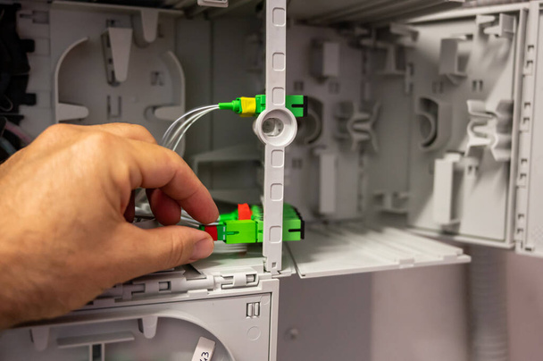 Een technicus aan het werk: close-up opname van de hand controleren van de bekabeling van de optische vezels in de distributiekast. - Foto, afbeelding