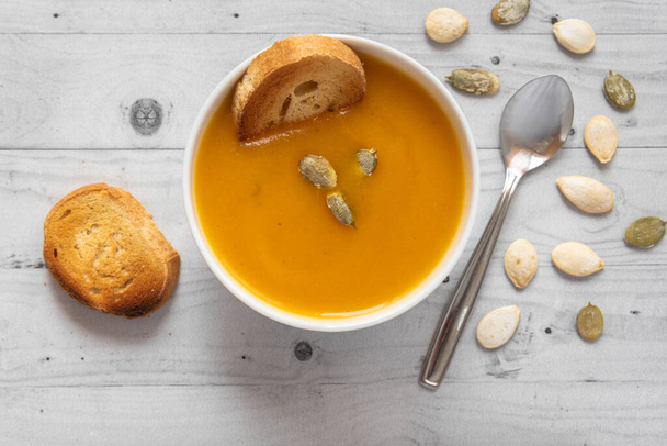 Pumpkin soup with bread on a light wooden background with spoon and seeds - Photo, Image