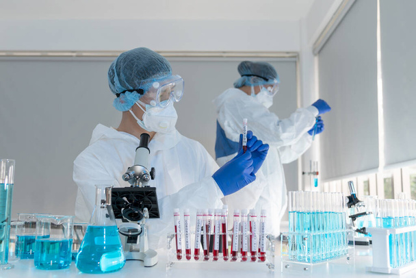 Ασιάτης επιστήμονας στο εργαστήριο κρατώντας ένα μολυσμένο σωλήνα αίματος covid-19. Ιολόγοι ερευνούν και εφηύραν το εμβόλιο αντισωμάτων για την πρόληψη μιας πανδημίας του coronavirus στο εργαστήριο - Φωτογραφία, εικόνα