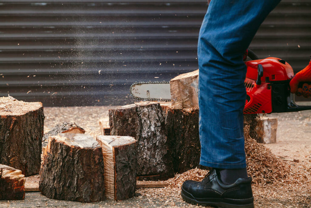 chainsaw is working. A man is sawing a piece of a tree trunk with a chainsaw. The piece stands on a large tree stump in the yard - Foto, imagen