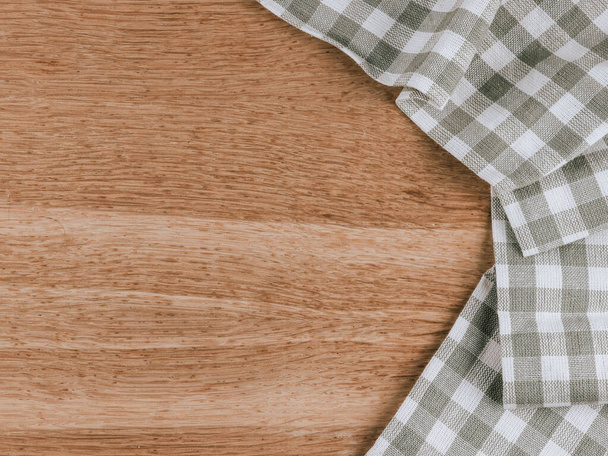 Une serviette de cuisine à carreaux se trouve à droite sur un fond en bois avec de l'espace pour le texte à gauche, vue de dessus gros plan. - Photo, image