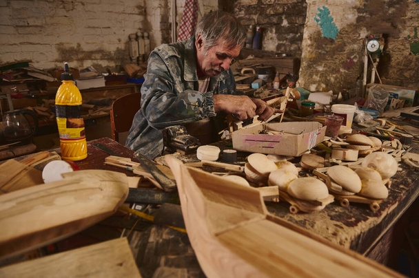 Homme mûr menuisier faisant des jouets en bois dans l'atelier, Artisanat en action, vieil artiste au travail - Photo, image