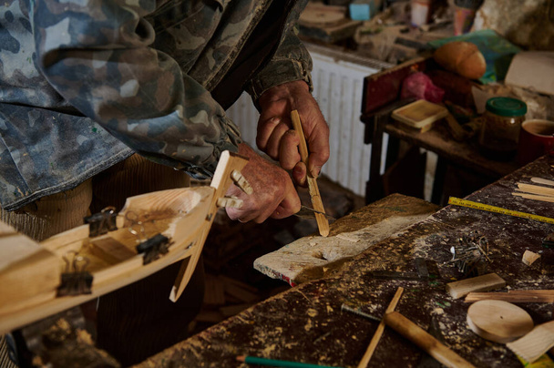 Falegname utilizzando strumenti per tagliare parte del materiale in legno per fare modello in legno di barca a vela. Artigiano che fa giocattoli artigianali in legno fatti a mano. Artigiano in azione - Foto, immagini