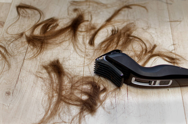 Ξυρισμένα μαλλιά και μια μηχανή ξυρίσματος στο πάτωμα.. - Φωτογραφία, εικόνα