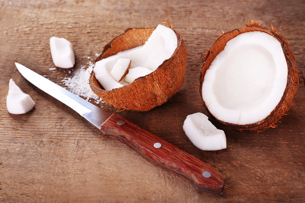 Broken coconut with knife on wooden background - 写真・画像