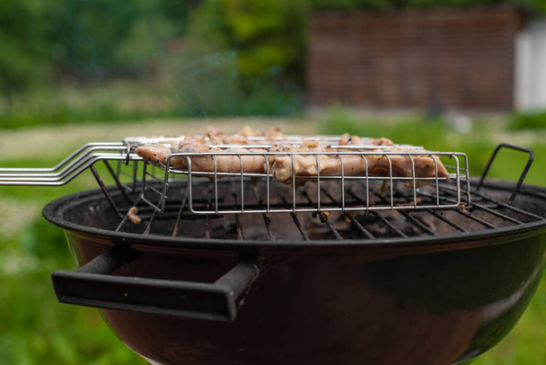 View of chicken meat on the grill. Grilling meat outside on a barbecue grill. Outdoor grill party in summer season. Sunny summer day. - Photo, Image