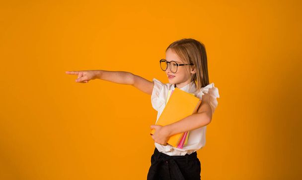 школьница в форме и очках стоит и указывает на сторону на желтом фоне с местом для текста. - Фото, изображение