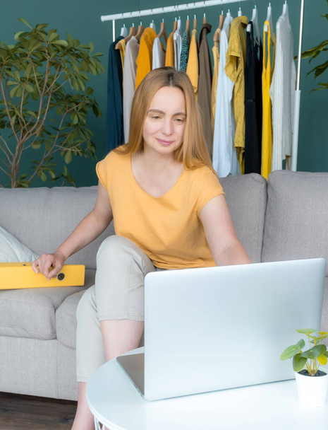 Középkorú szőke nő ül a kanapén, és kommunikál online Laptop. - Fotó, kép