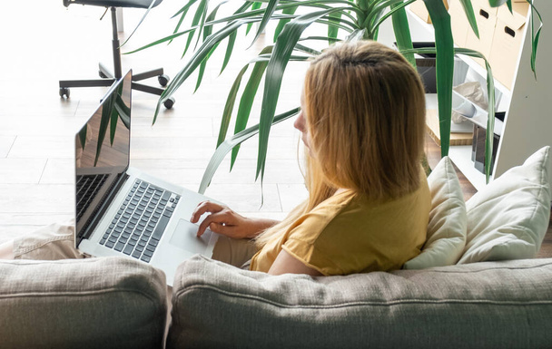 Блондинка среднего возраста сидит на диване и общается онлайн с ноутбуком. - Фото, изображение