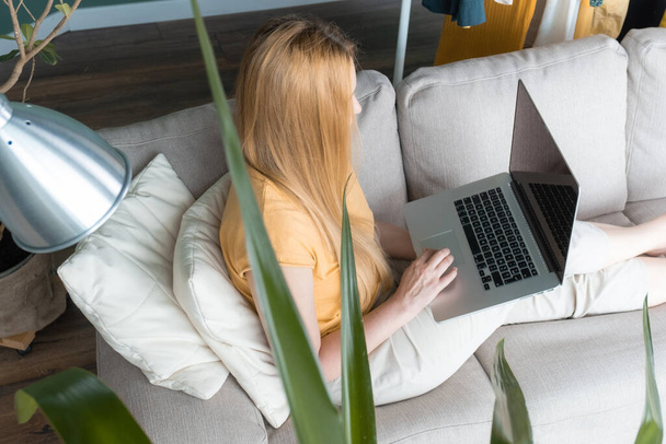 Donna Bionda di mezza età seduta sul divano e comunica online con Laptop. - Foto, immagini