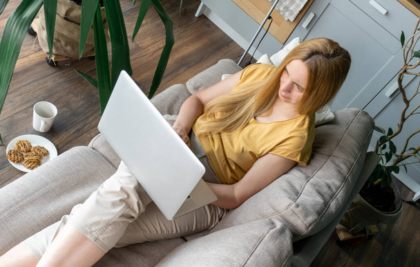 Middle Aged Blond Woman sitting on the sofa and communicates online by Laptop. - Zdjęcie, obraz
