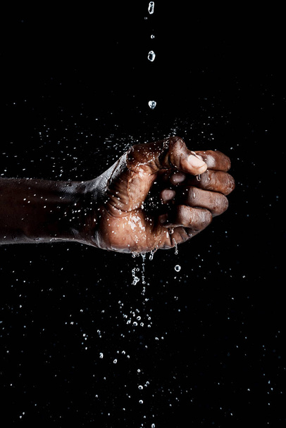Afrikaanse man hand interactie met water en zwarte achtergrond. - Foto, afbeelding