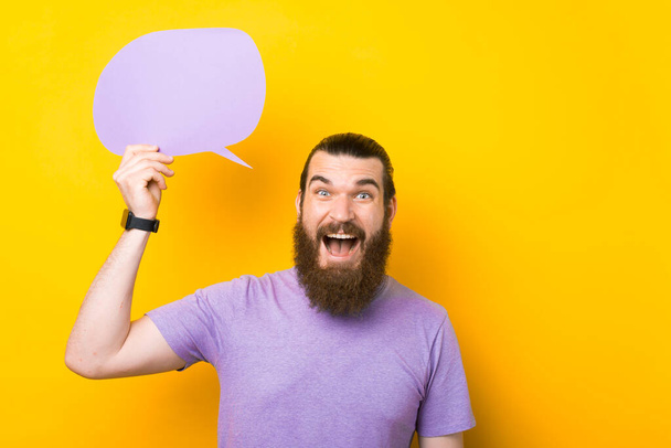 Excited bearded man holding speech bubble with empty space for text on yellow background - Fotografie, Obrázek