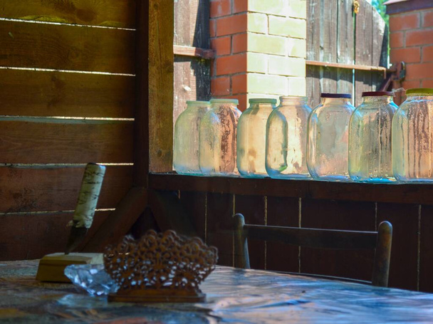 Puste szklane zbiorniki z kolorowymi pokrywami stoją na drewnianym balustradzie przy stole - Zdjęcie, obraz