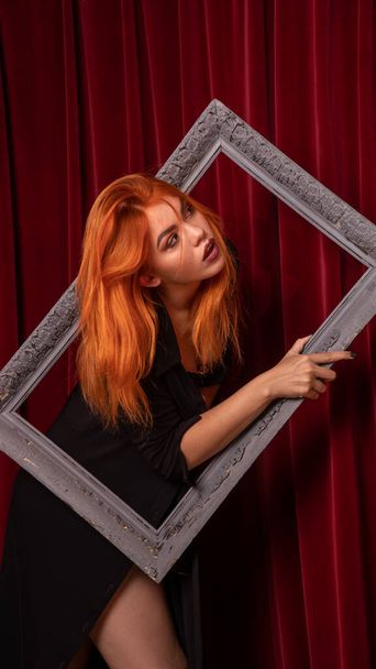 young Red-haired woman posing with empty antique frames on red background  - Foto, immagini