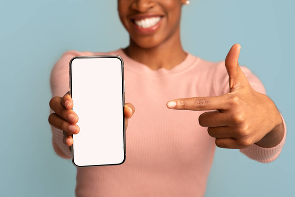 Mosolygó fekete hölgy rámutatva Smartphone üres fehér képernyő a kezében - Fotó, kép
