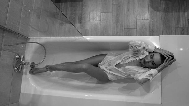 красивая молодая женщина в мужской рубашке позирует в ванной комнате, черно-белое фото - Фото, изображение