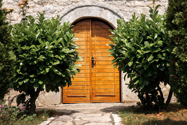 ξύλινες πόρτες πέτρινου σπιτιού που περιβάλλεται από δάφνες. - Φωτογραφία, εικόνα