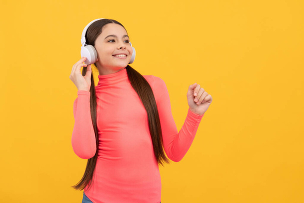 happy teen girl listen music in headphones on yellow background, copy space, digital device - Photo, Image
