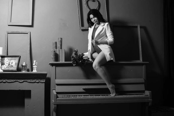 beautiful brunette woman in blazer and white angel wings posing near piano at studio  - Zdjęcie, obraz