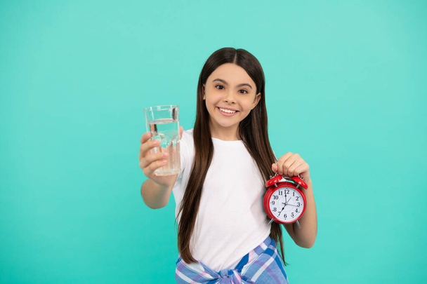 щаслива дівчина-підліток тримає склянку води і будильник, щоб зберегти щоденний баланс води вчасно, пити воду
 - Фото, зображення