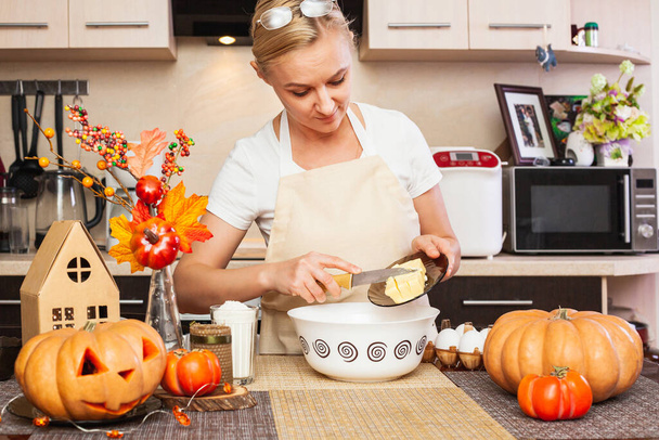 Eine Frau legt in der herbstlich dekorierten Küche Butter in den Plätzchenteig für Halloween. Gemütliches Zuhause und Vorbereitung. Plätzchen backen für Halloween. - Foto, Bild