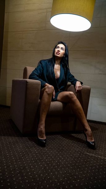 una hermosa mujer joven sexy vestida con una chaqueta y tacones altos posando en la habitación - Foto, imagen