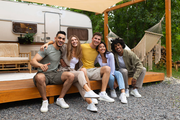Full length portret van multiraciale jonge vrienden zitten in de buurt van camper, glimlachen op camera buiten - Foto, afbeelding