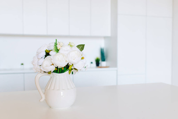 Soft home decor, white jug, vase with white  beautiful flowers on a white wall background and on a wooden shelf. Interior. - Foto, Imagem