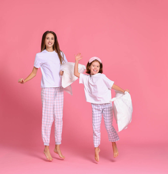 Αισιόδοξη νεαρή γυναίκα και κορίτσι με μαξιλάρια που σηκώνουν τα χέρια και πηδούν πάνω σε ροζ φόντο το πρωί - Φωτογραφία, εικόνα