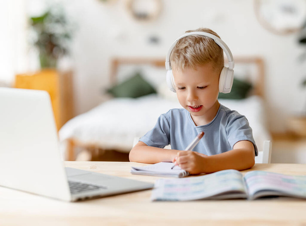 集中した子供の男の子は自宅でオンラインレッスン中にビデオ通話をしながら先生を注意深く見ます - 写真・画像