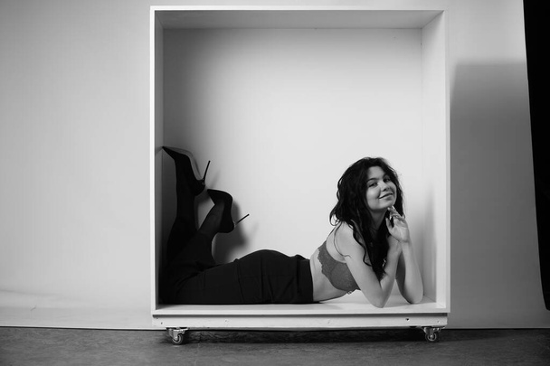 bela morena mulher vestindo lingerie e calças posando em cubo branco no estúdio  - Foto, Imagem