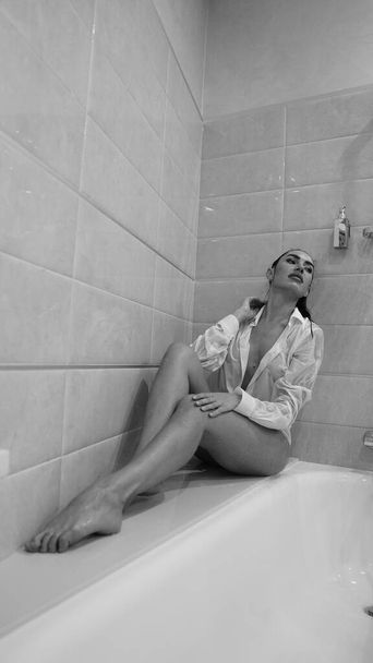 beautiful young woman in male shirt posing in the bathroom, black and white photo - Photo, Image
