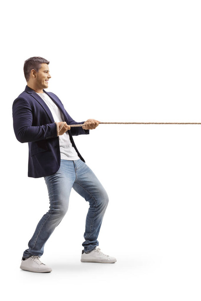 Full length profile shot of a young casual man pulling a rope isolated on white background - Foto, imagen