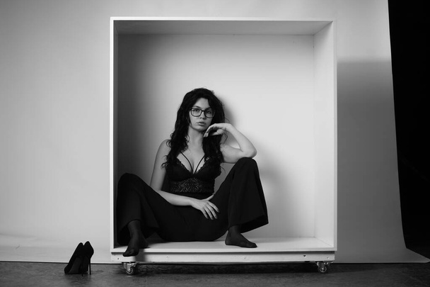 belle femme brune portant lingerie et pantalon posant en cube blanc au studio  - Photo, image