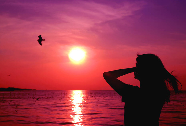 Uçan bir kuşla canlı pembe gündoğumu gökyüzüne bakan bir kadın silueti. - Fotoğraf, Görsel