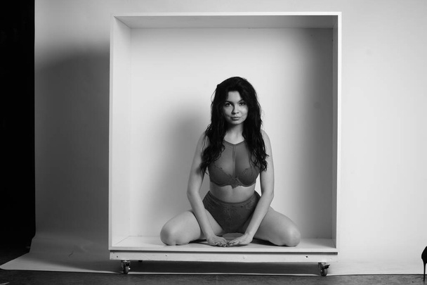 hermosa morena mujer usando lencería posando en cubo blanco en el estudio  - Foto, Imagen