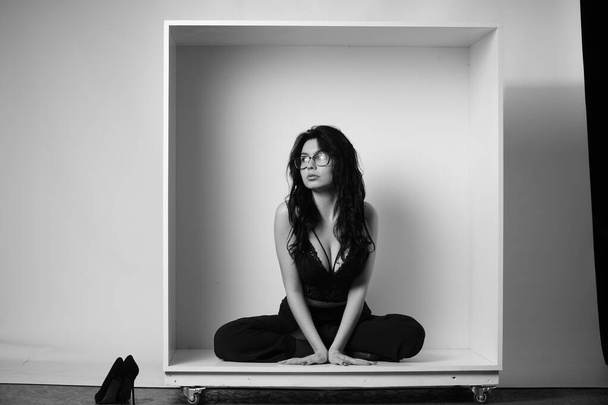 bella donna bruna che indossa lingerie e pantaloni in posa in cubo bianco in studio  - Foto, immagini