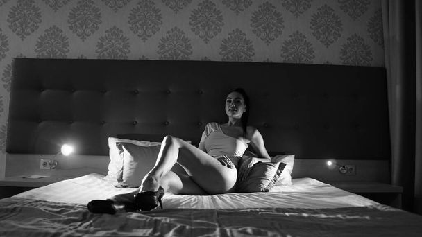 красивая молодая женщина в телесном костюме позирует на кровати в комнате, черно-белое фото - Фото, изображение
