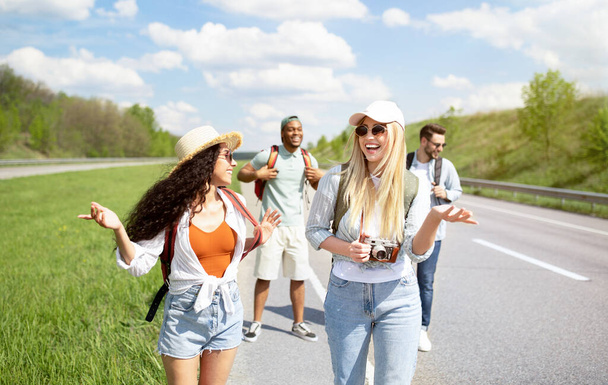 Giovani amici diversi con zaini che camminano lungo la strada, viaggiano insieme, hanno viaggio autostop - Foto, immagini