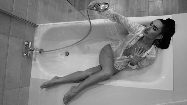 красивая молодая женщина в мужской рубашке позирует в ванной комнате, черно-белое фото - Фото, изображение