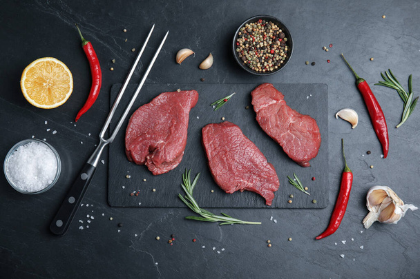 Fresh raw meat steaks and spices on black table, flat lay - Φωτογραφία, εικόνα