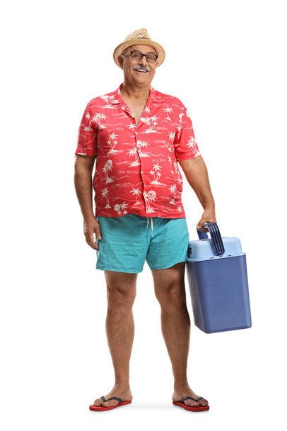 Full length portrait of a mature male tourist holding a portable fridge isolated on white background - Foto, imagen