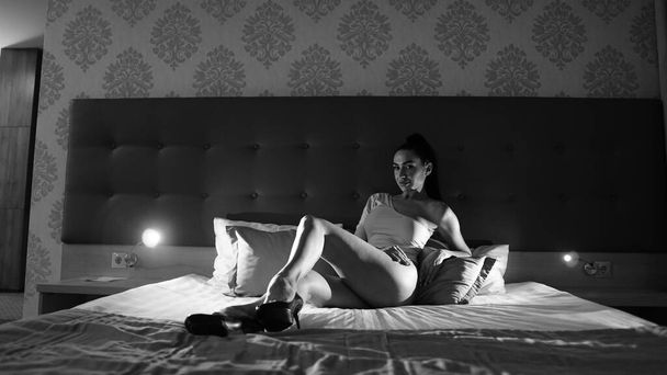 bela jovem mulher em bodysuit posando na cama no quarto, foto preto e branco - Foto, Imagem