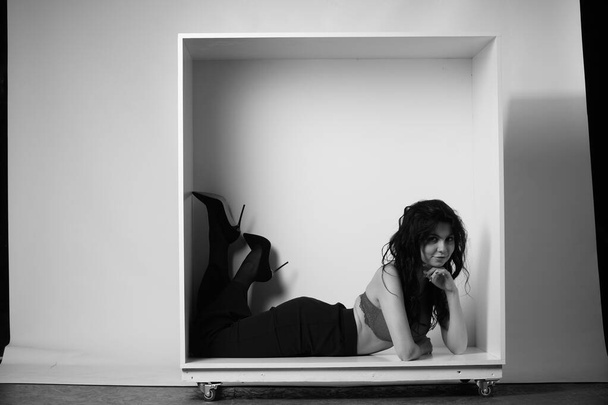 hermosa mujer morena con lencería y pantalones posando en cubo blanco en el estudio  - Foto, Imagen