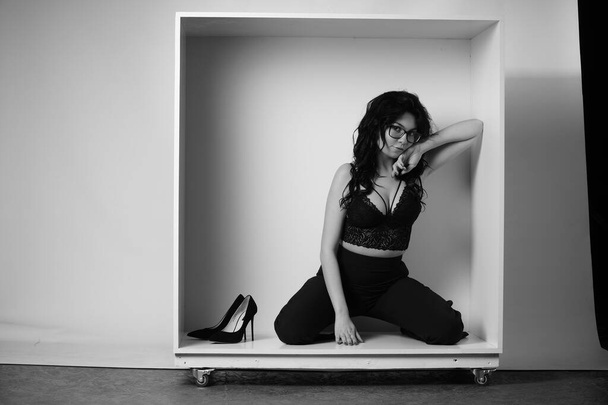 hermosa mujer morena con lencería y pantalones posando en cubo blanco en el estudio  - Foto, Imagen